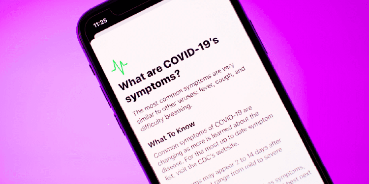 A smartphone screen displays information about COVID-19 symptoms, including fever, cough, and difficulty breathing, against a purple background.