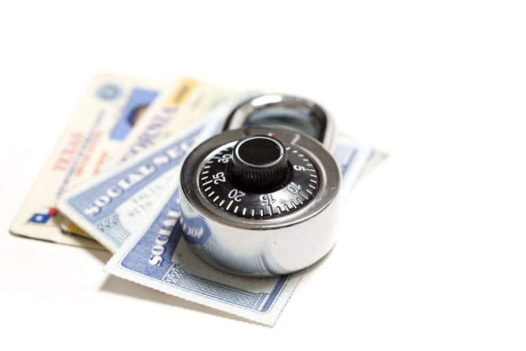 A combination padlock sits on top of several Social Security cards and a birth certificate on a white background.