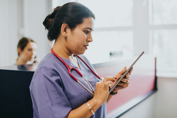 urgent care nurse in purple scrubs reviewing information on a tablet