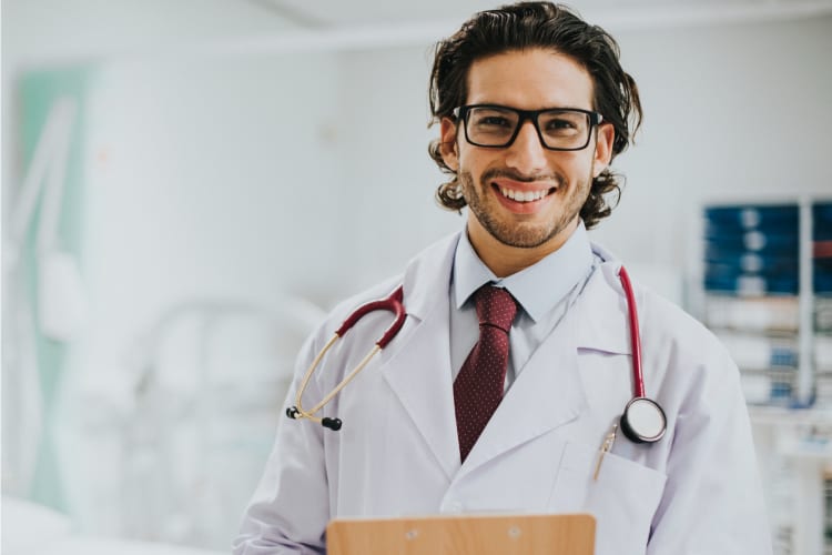 young doctor in a white lab coat smiling into the camera