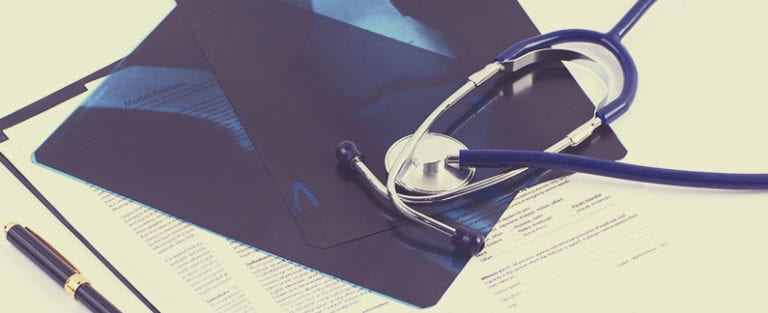 A stethoscope, X-ray films, and documents lay on a desk next to a pen.