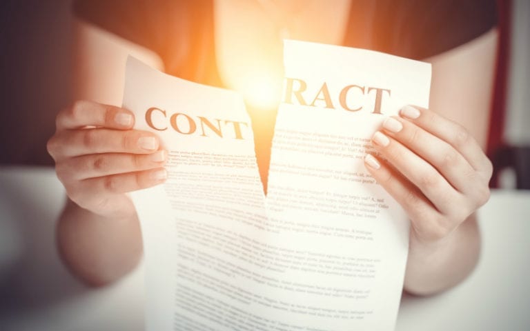 A person tears a contract in half, holding each piece in their hands.