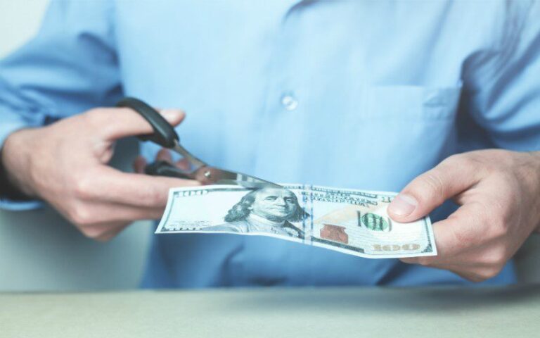 A person uses scissors to cut a $100 bill in half.