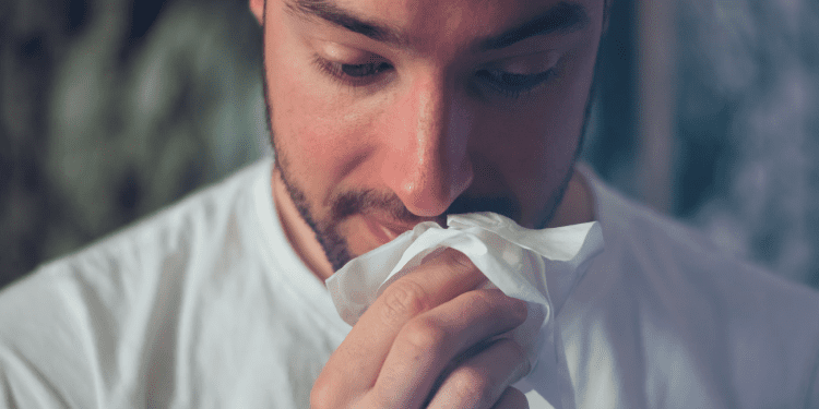 A man holds a tissue to his nose, appearing to wipe or blow his nose, possibly due to a cold or allergies.