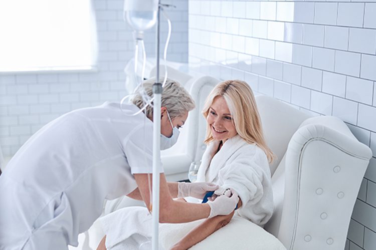 Pretty Lady Sitting In Chair While Nurse Getting An Intravenous Vitamin Drip Treatment In Beauty Clinic