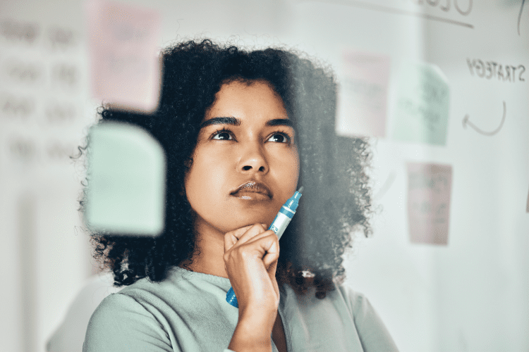 A person holding a marker looks thoughtful while staring at notes and writing on a transparent board.