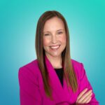 A woman with straight brown hair, wearing a bright pink blazer, stands with arms crossed and smiles at the camera against a blue gradient background.